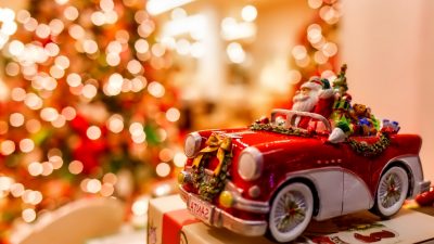Weihnachtsmann im Spielzeug-Auto vor Christbaum